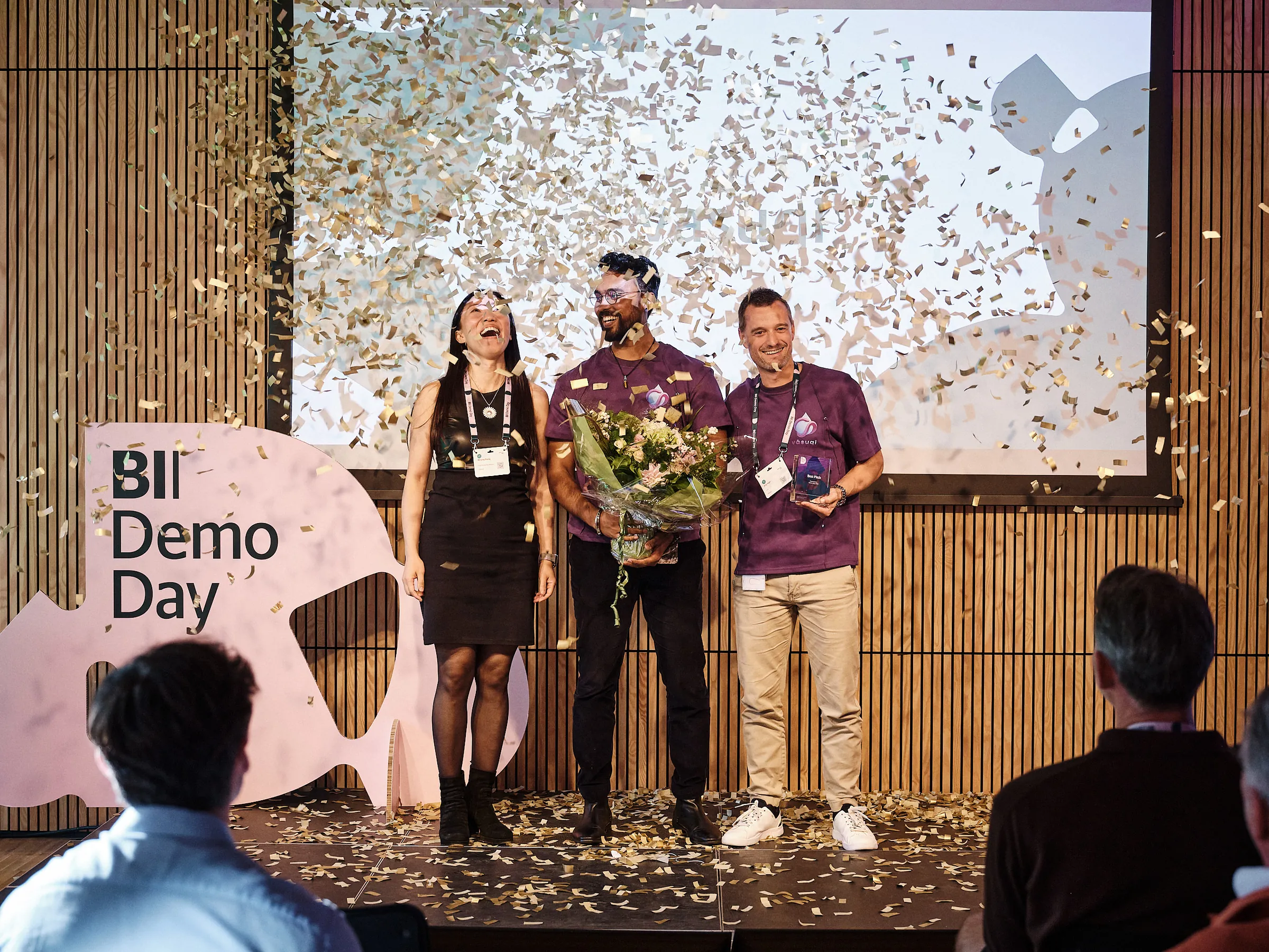 The Vāsuqi team on stage under falling confetti, with flowers and the award